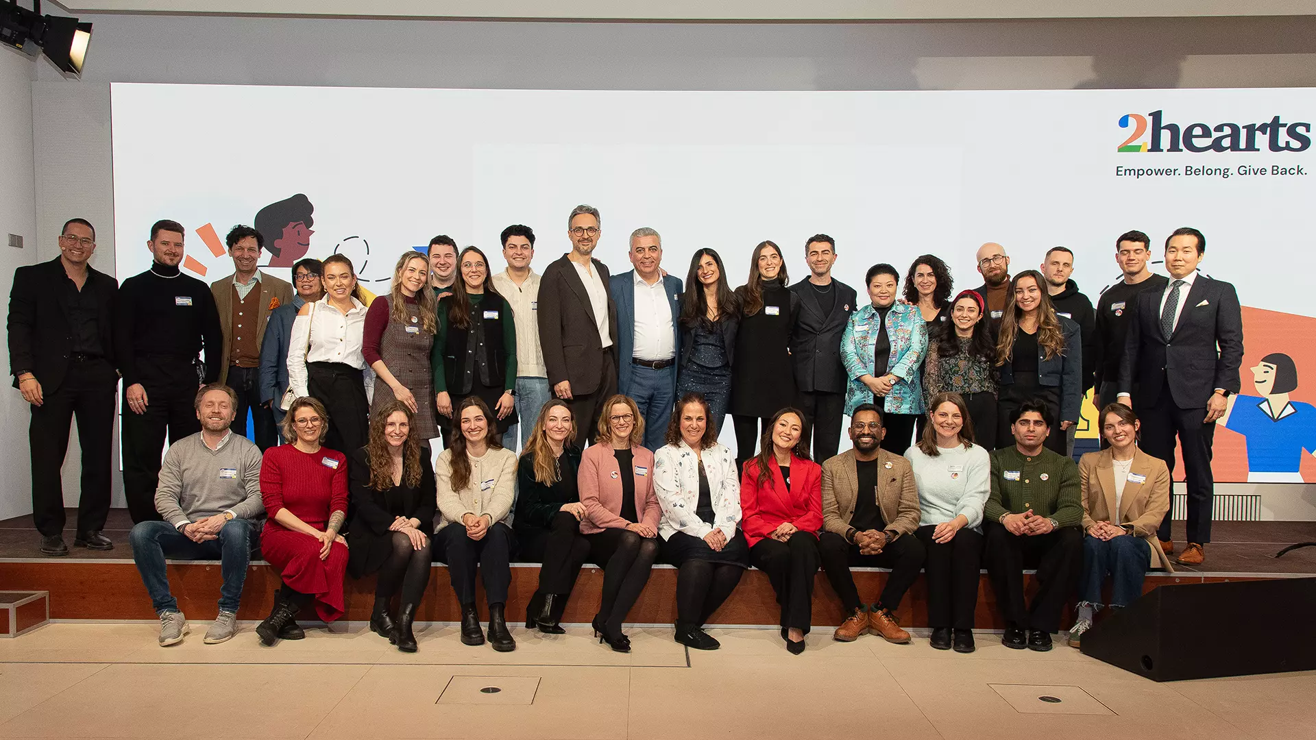 34 people are sitting and standing in two rows in front of a white background with the words “2hearts” written on it.