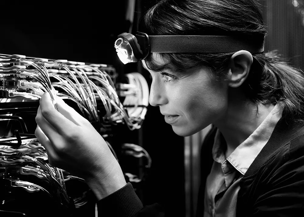 Person mit Stirnlampe prüft Kabelverbindungen in Serverrack in technischer Umgebung.