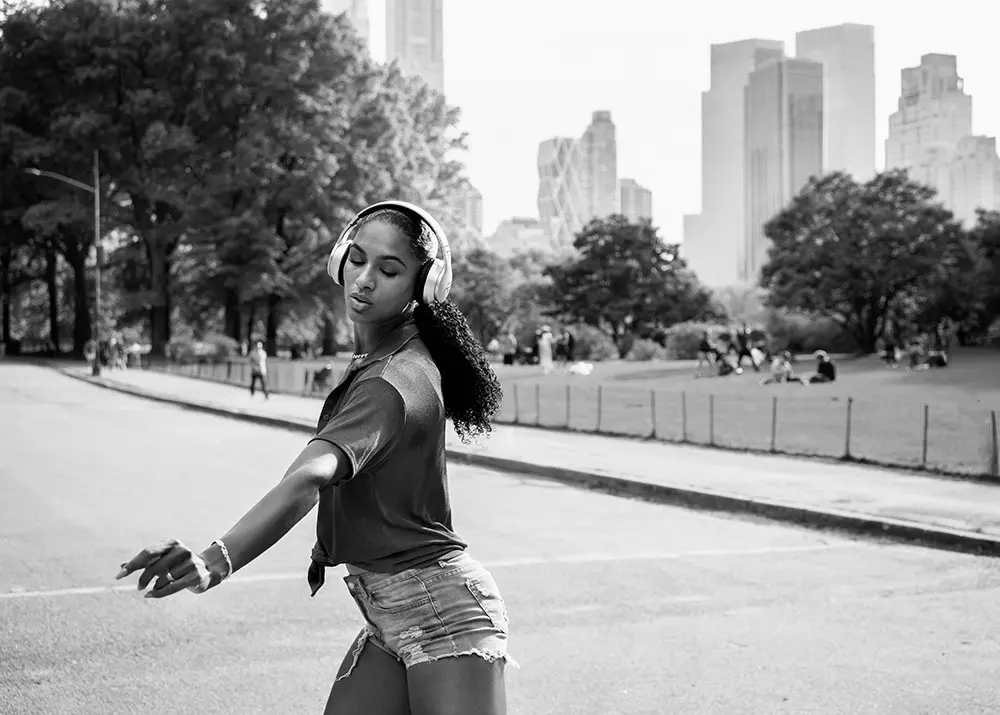 Person mit Kopfhörern im Central Park in New York, im Hintergrund Hochhäuser.