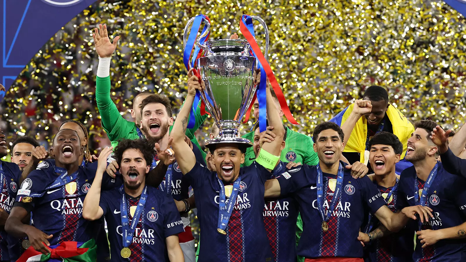 Several soccer players are standing in a shower of confetti, cheering. The player in the middle is holding a trophy aloft.