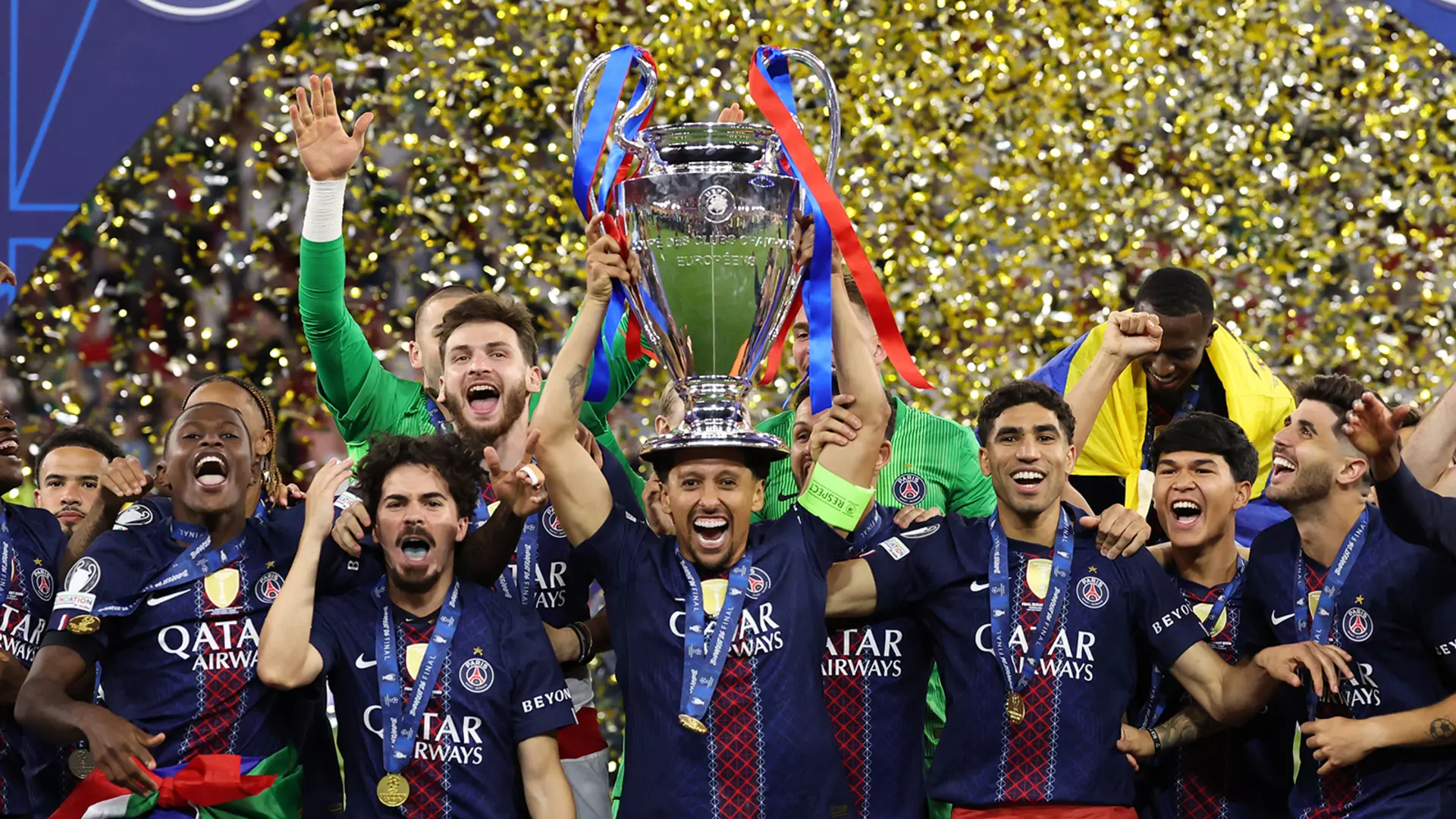 Several soccer players are standing in a shower of confetti, cheering. The player in the middle is holding a trophy aloft.