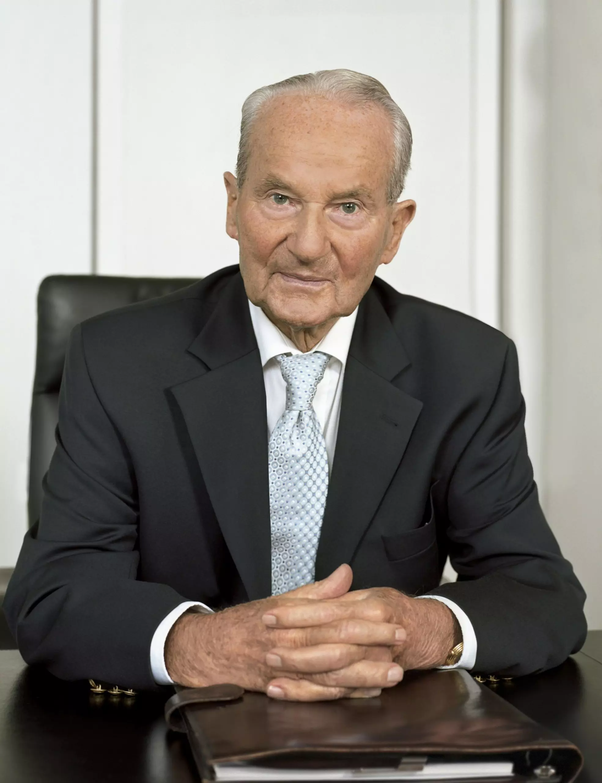 Portrait of Reinhard Mohn sitting at his desk, with a leather-bound work folder in front of him.