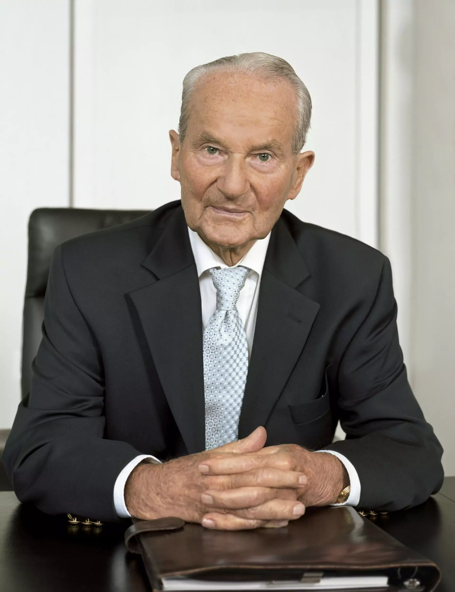 Portrait of Reinhard Mohn sitting at his desk, with a leather-bound work folder in front of him.