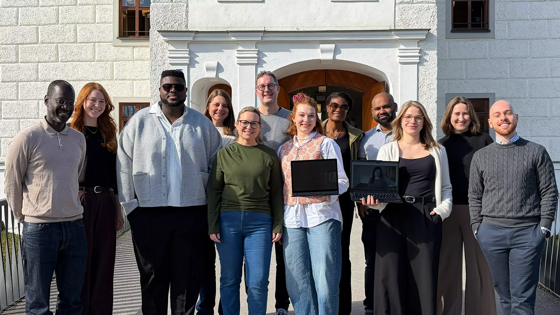 Twelve people are standing in front of a building
