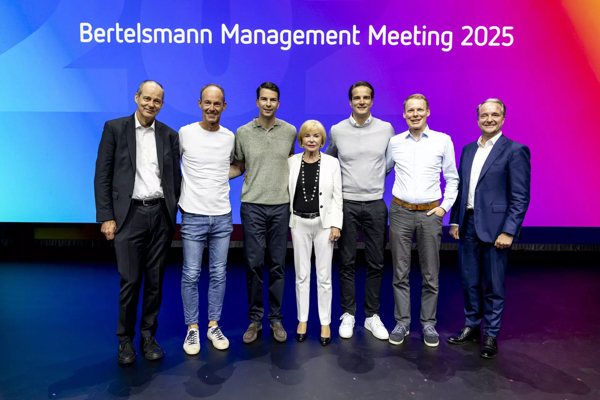 Sieben Personen stehen gemeinsam auf Bühne vor Leinwand mit Schriftzug „Bertelsmann Management Meeting 2025“.
