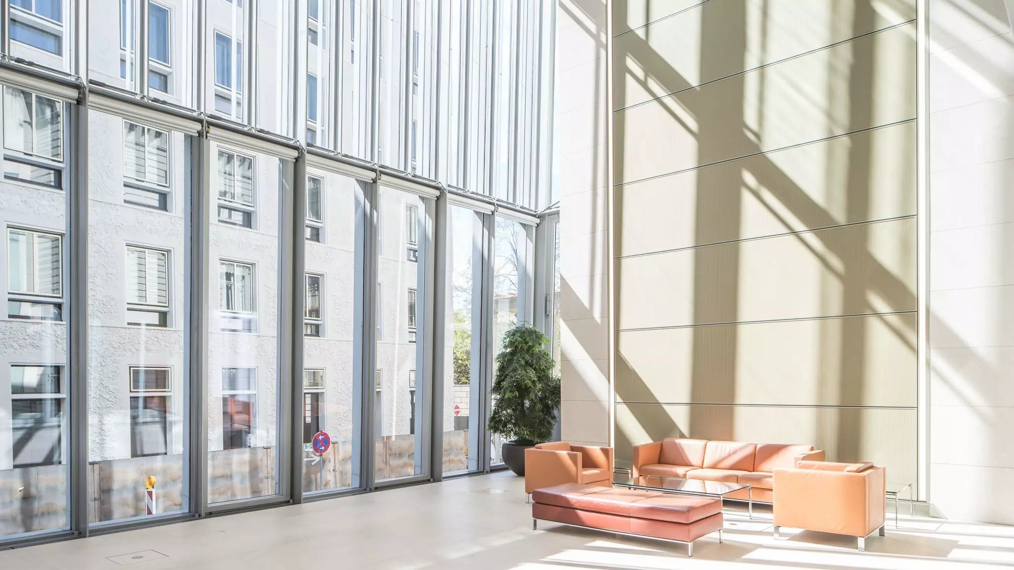 Heller Wintergarten mit bodentiefen Glasflächen, hohen Wänden, Sitzgruppe aus Sofas und viel Tageslicht.