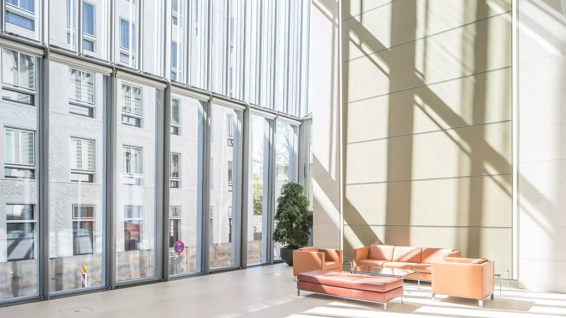 Heller Wintergarten mit bodentiefen Glasflächen, hohen Wänden, Sitzgruppe aus Sofas und viel Tageslicht.