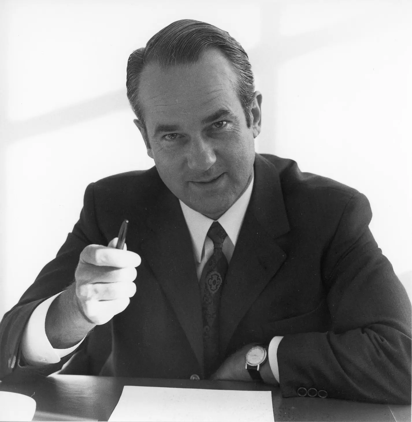 Reinhard Mohn sitting at his desk with a pen in his hand, a document in front of him.