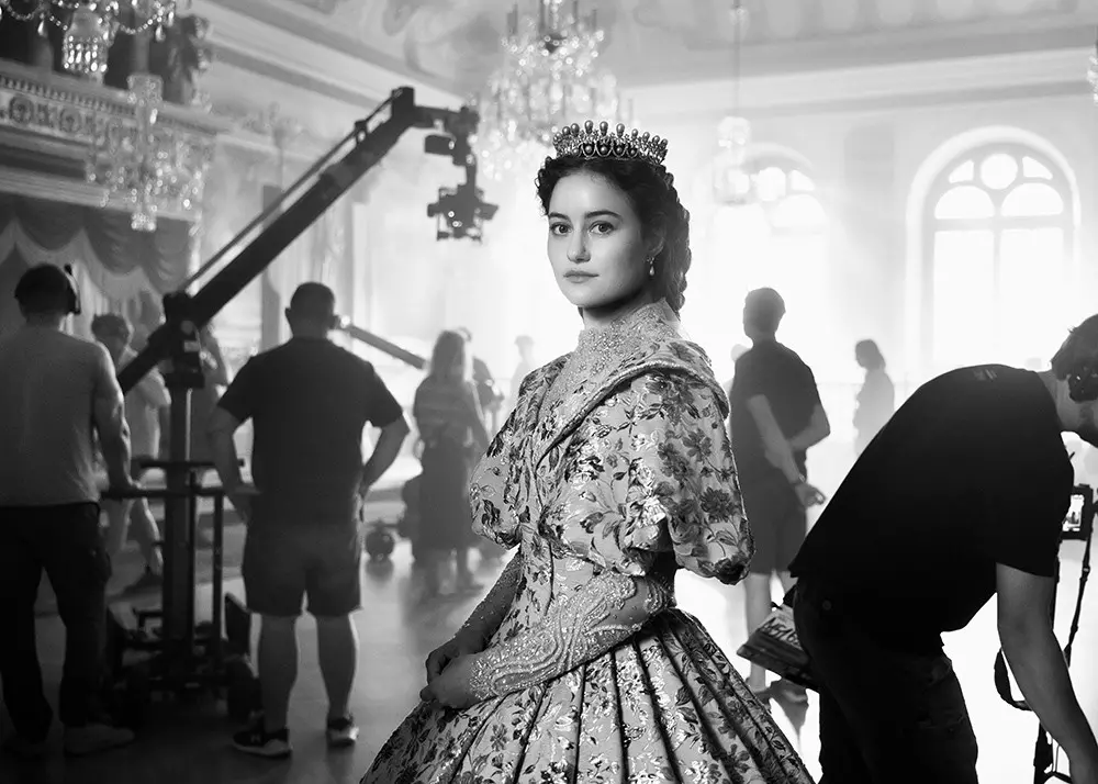 Darstellerin der Kaiserin Sissi steht im Kostüm am Filmset im Raum eines Schlosses, im Hintergrund ein Schwenkarm mit Filmkamera und mehrere Crewmitarbeitende.