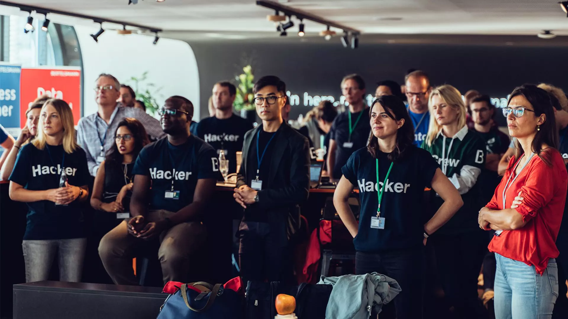 Gruppe von Teilnehmenden in schwarzen Hacker-T-Shirts verfolgt eine Präsentation in einem Veranstaltungsraum.