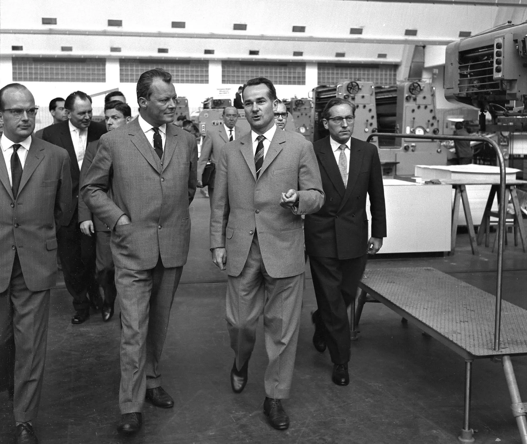 Several people walk through a hall containing machines.