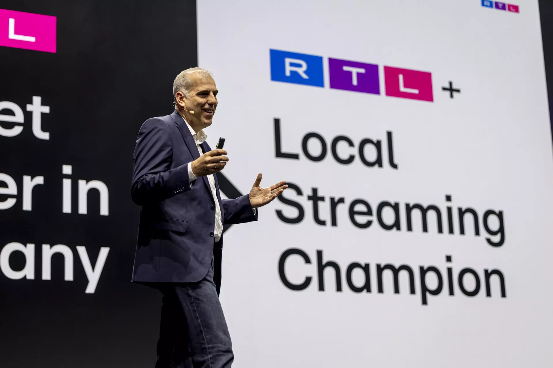 Person im Anzug spricht auf Bühne vor Folie mit Schriftzug „RTL+ Local Streaming Champion“.