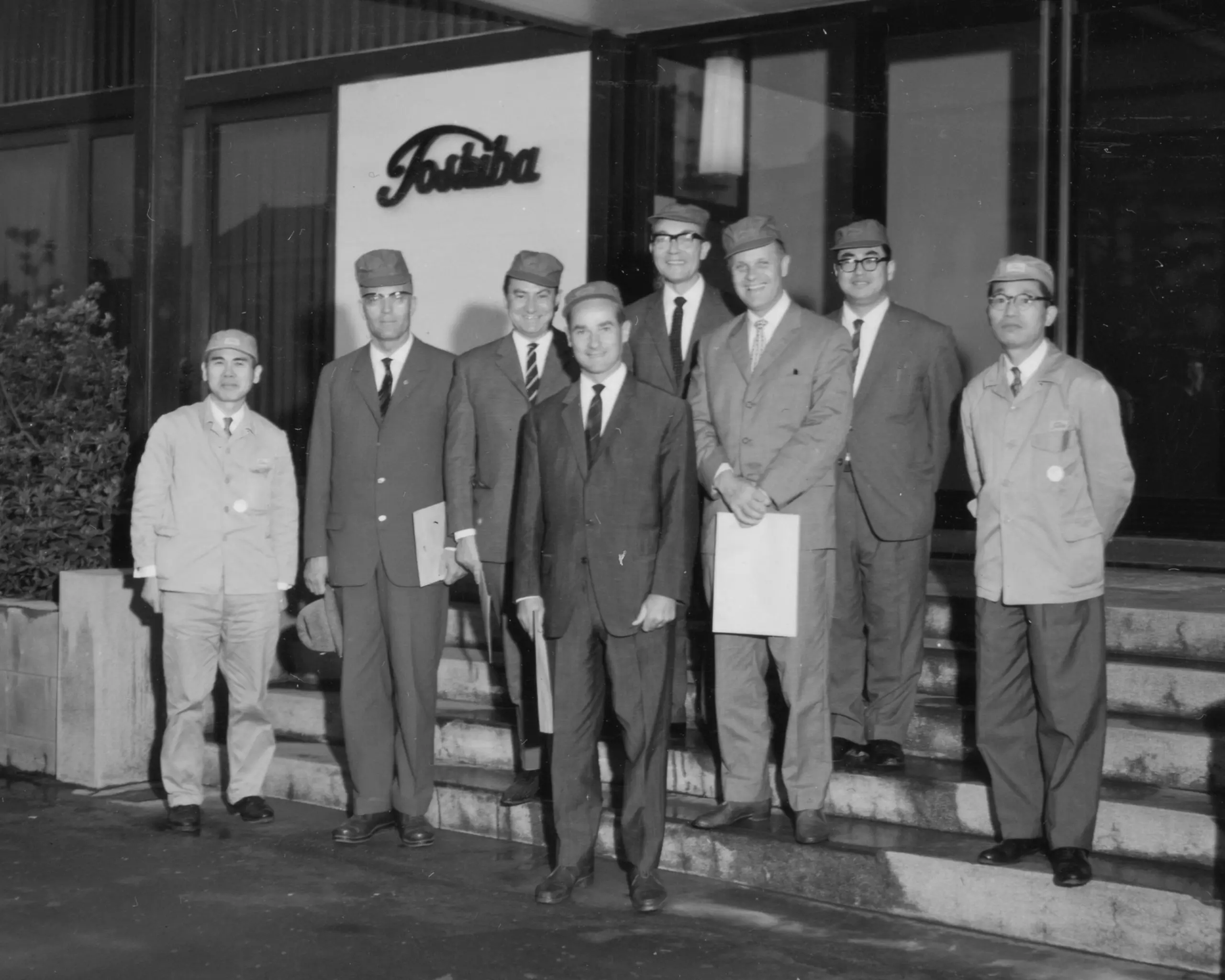 A group of eight people standing on the steps in front of a building bearing the company name "Toshiba".