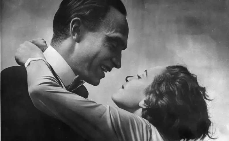 Dunkelhaariger Mann und Frau mit Bubikopf stehen eng umschlungen; sie blicken sich intensiv an, er lächelt, ihr Arm liegt um seinen Nacken, intime Schwarz-Weiße Stummfilmszene.