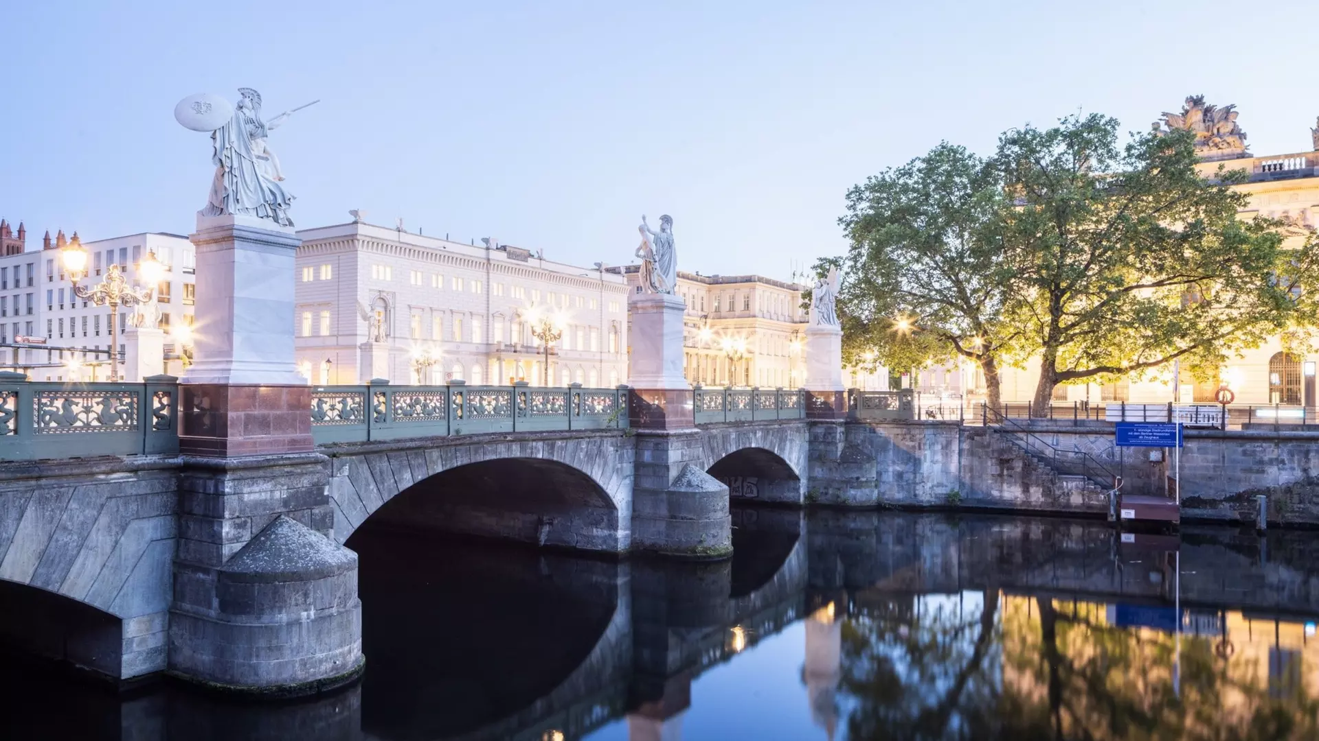 Beleuchtete klassizistische Gebäudezeile bei Dämmerung, breite Straße mit Lichtspuren und Laternen im Vordergrund