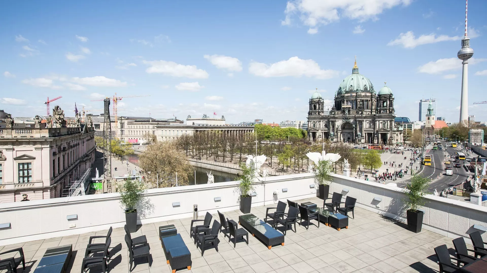 Dachterrasse mit Sitzmöbeln, Blick über die Spree zur Berliner Domkuppel, Museumsbauten und Fernsehturm bei Tageslicht.