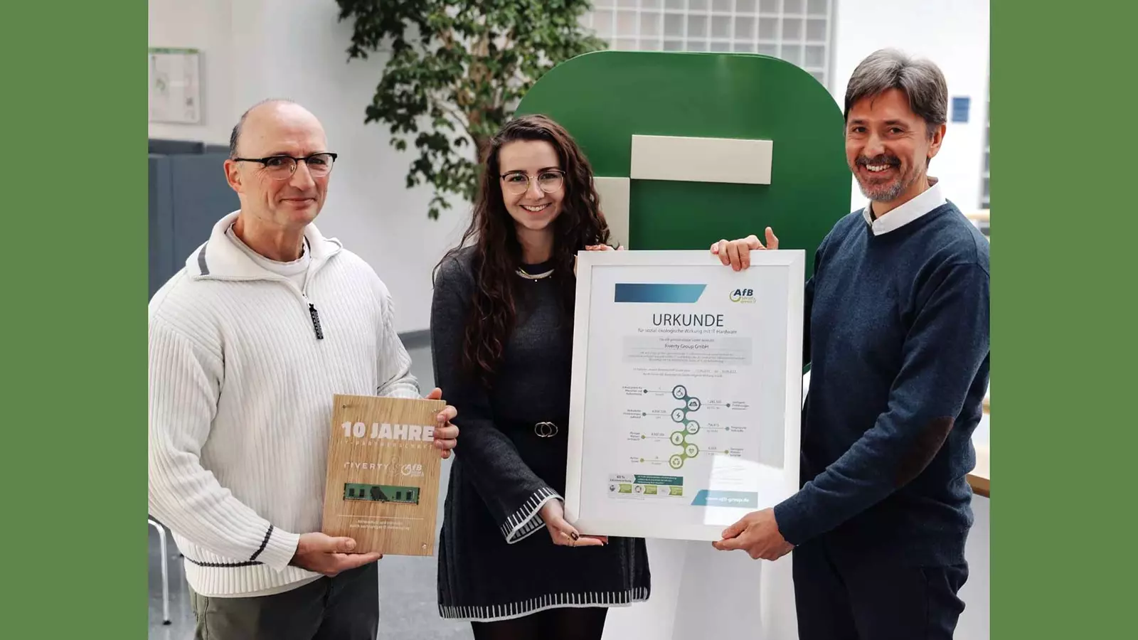 Three people hold a ten‑year anniversary plaque and a framed certificate in front of a large green Riverty logo.