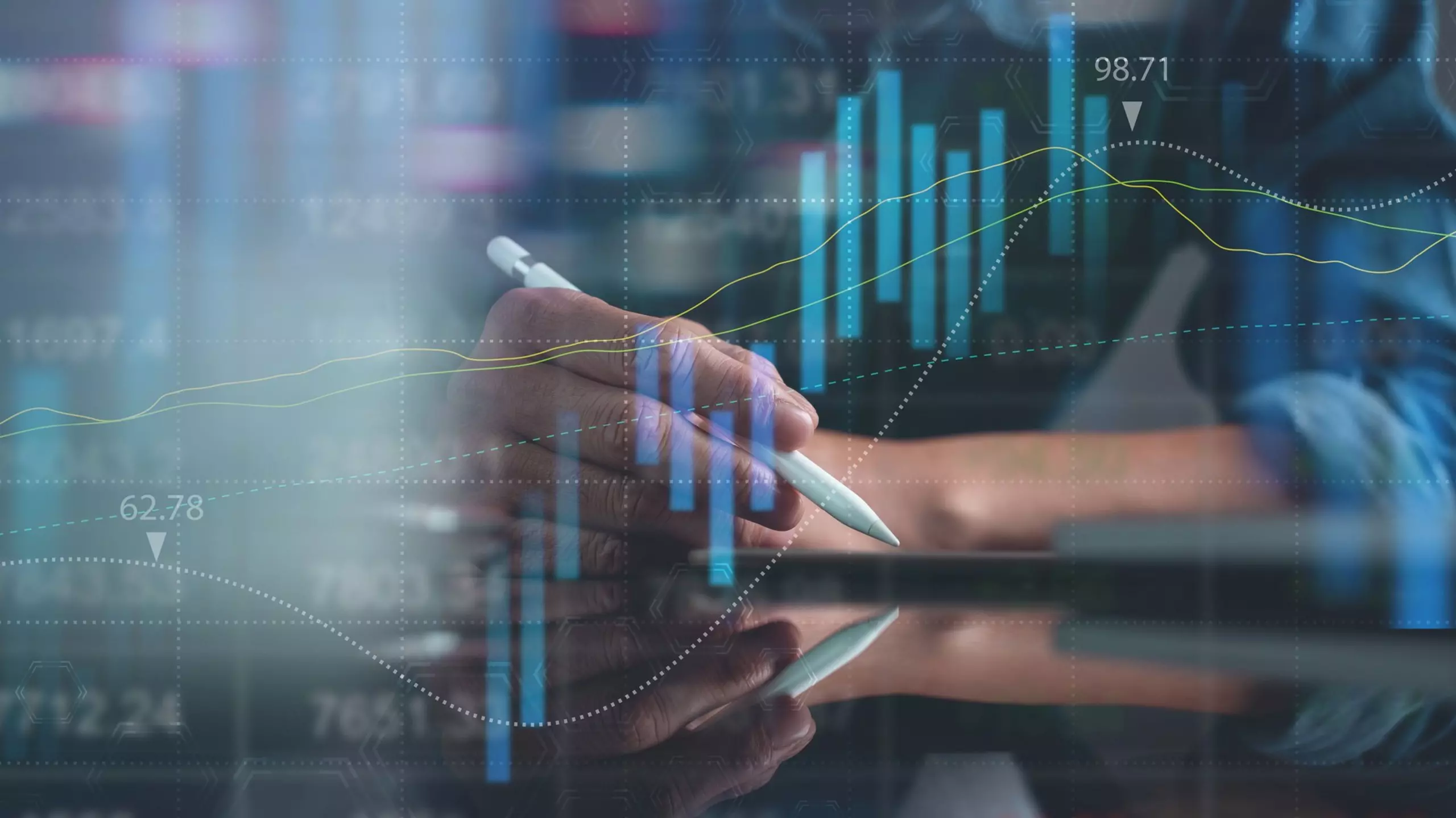 Hand holding a pen in front of overlaid financial charts.
