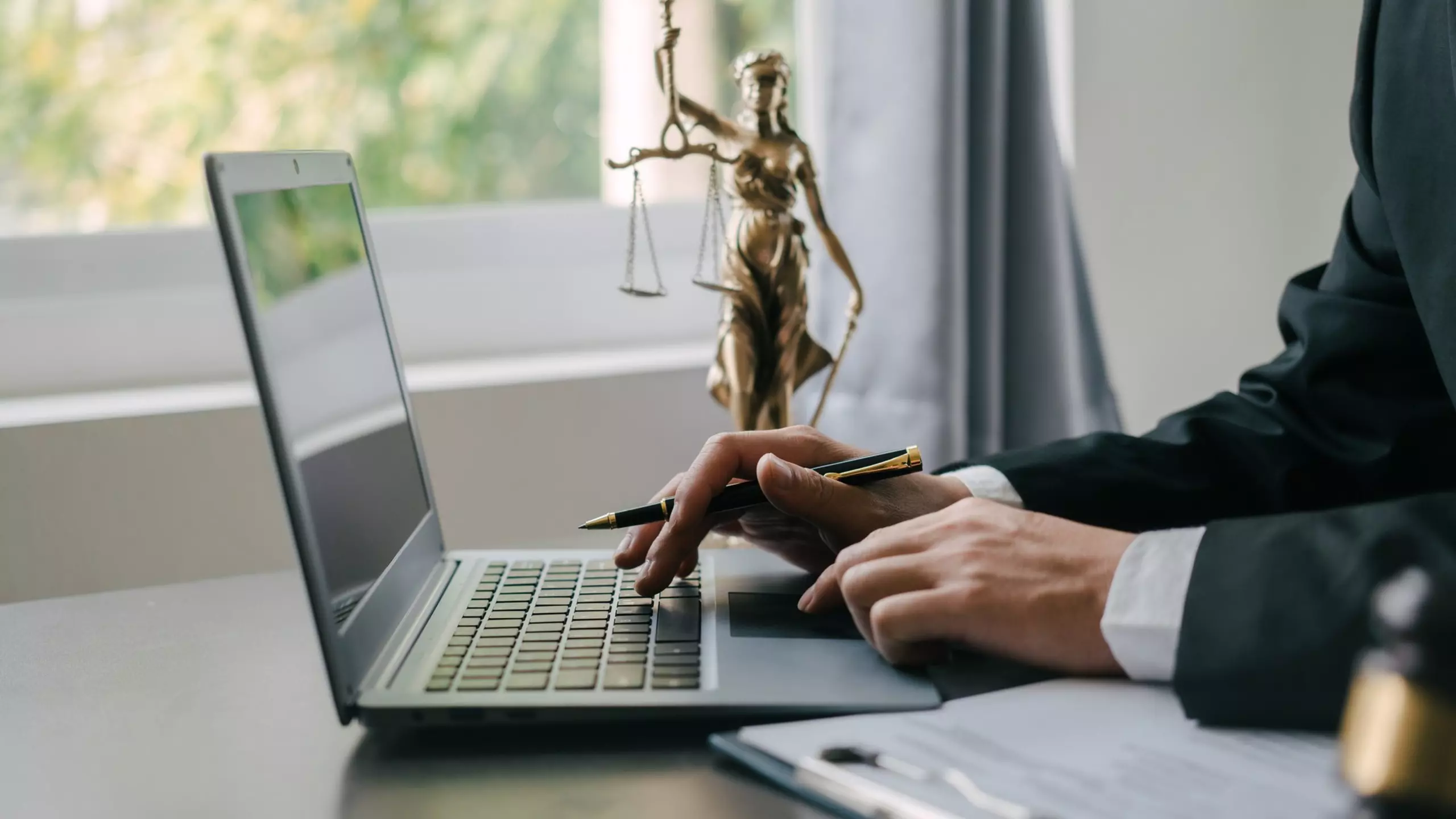 Person working on a laptop with a Lady Justice statue in the background.