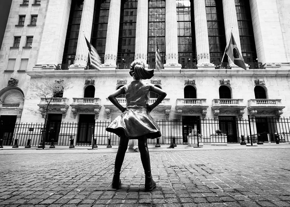 Bronzestatue eines Mädchens vor Säulenfassade mit US-Flaggen an historischer Börsenfassade.