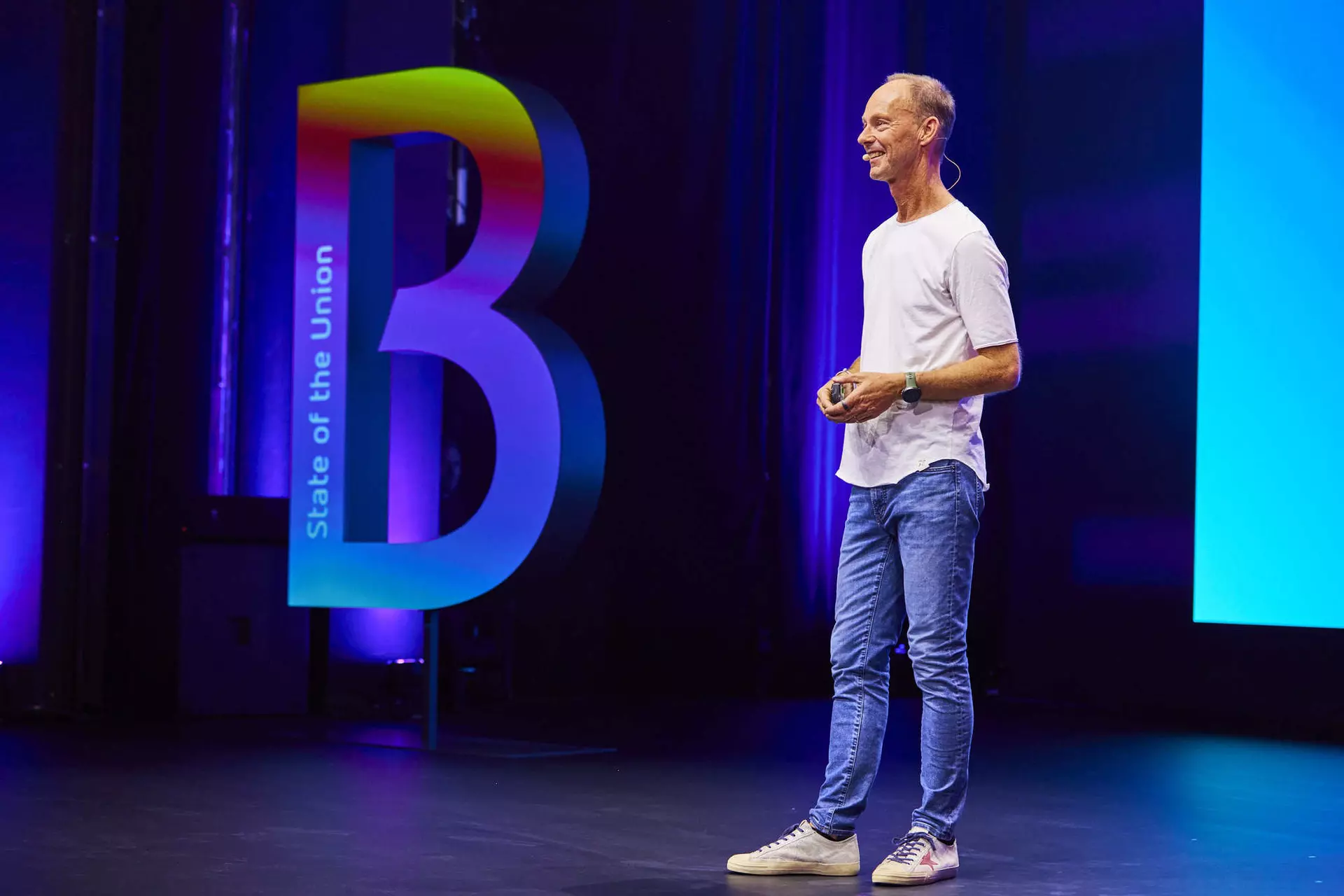 Person im T-Shirt steht auf Bühne neben großem farbigem Buchstaben „B“ mit Schriftzug „State of the Union“.