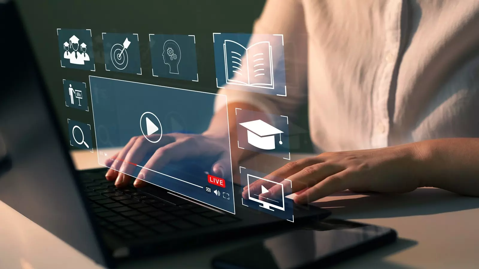 Person arbeitet am Laptop; digitale Lern- und Medien-Icons schweben als Hologramm über der Tastatur.