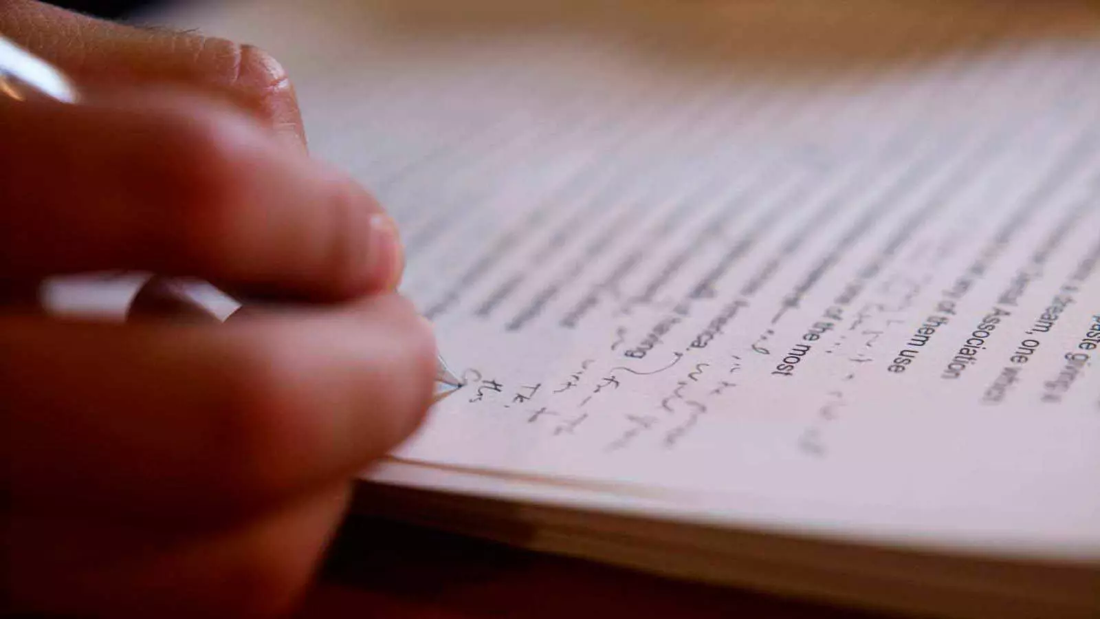 One hand holds a pen and takes notes on a script.