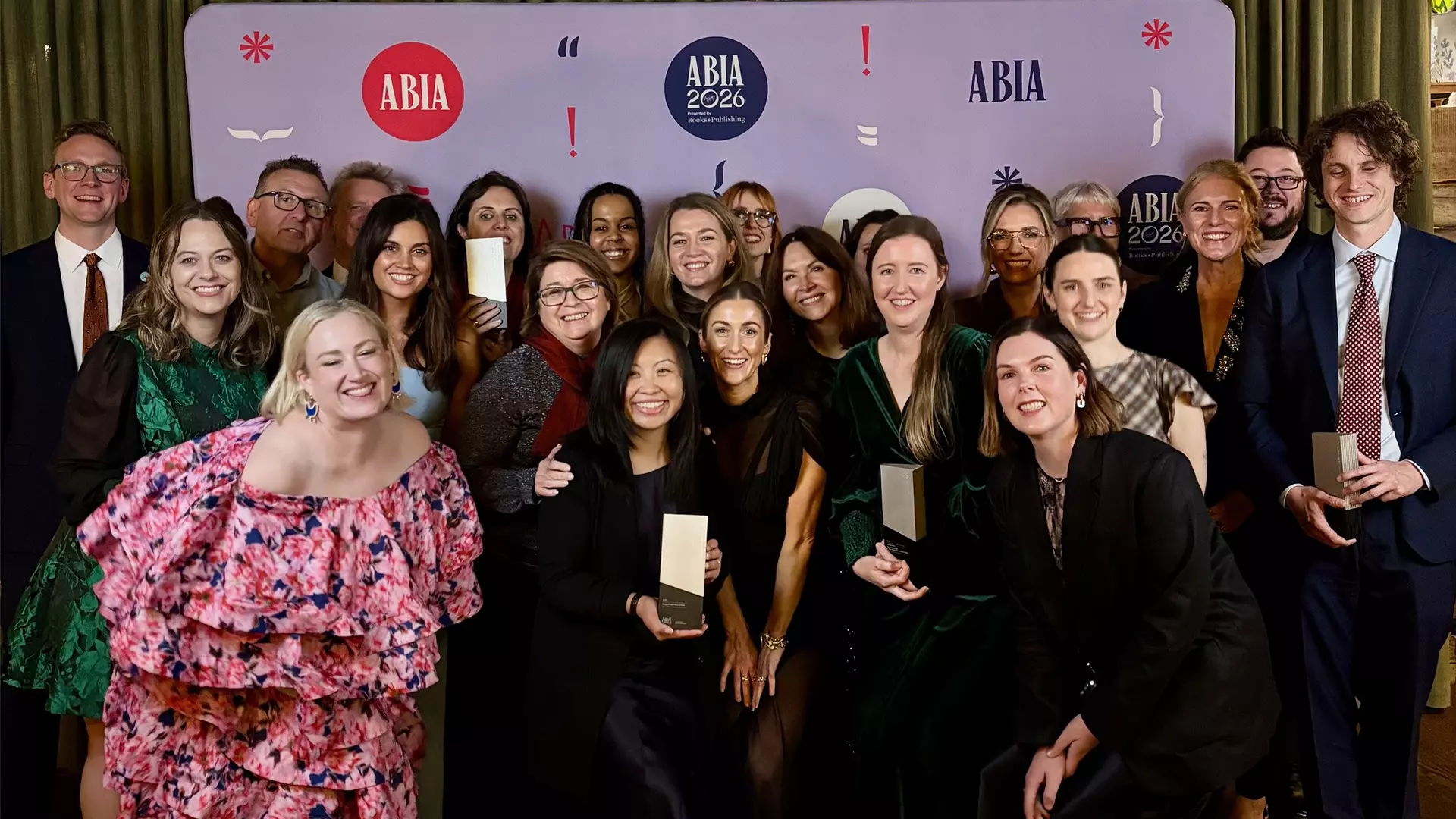 A group of people is standing in front of a wall covered with logos. Some of them are holding awards in their hands.