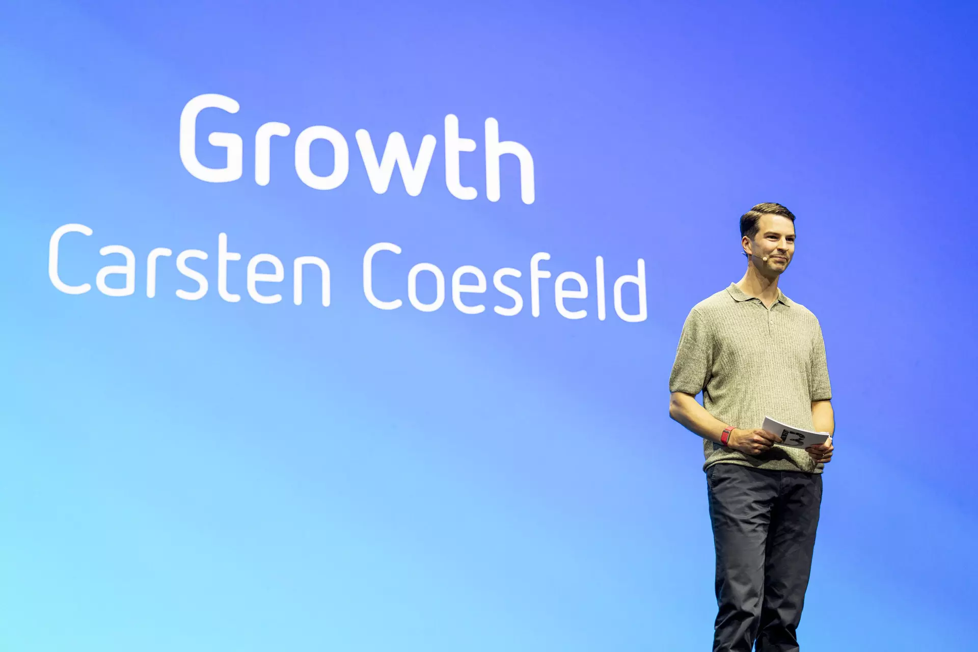 Person steht auf Bühne vor blauer Leinwand mit Schriftzug „Growth - Carsten Coesfeld“.