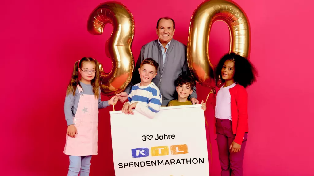 Wolfram Kons stands behind the poster with four children: 30 years of the RTL charity marathon. They have a 30 made of golden balloons standing between them.