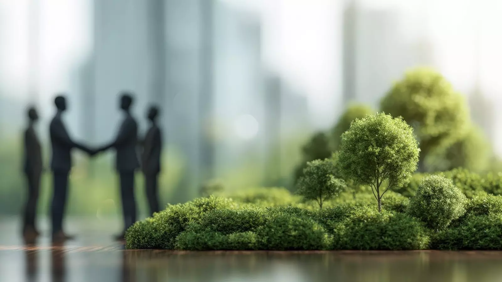Miniaturlandschaft mit Bäumen im Vordergrund; unscharfe Personen reichen sich die Hand im Hintergrund.