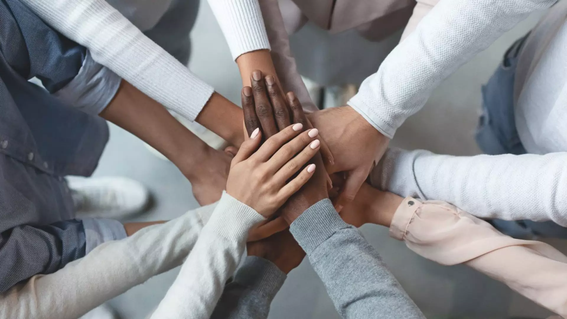 Twelve hands of different skin colors stacked on top of each other