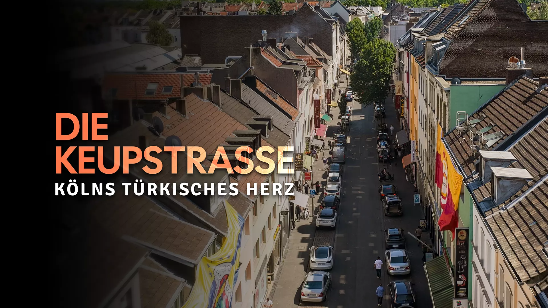 A street lined with many houses of different colors. There are parked cars on both sides of the street.