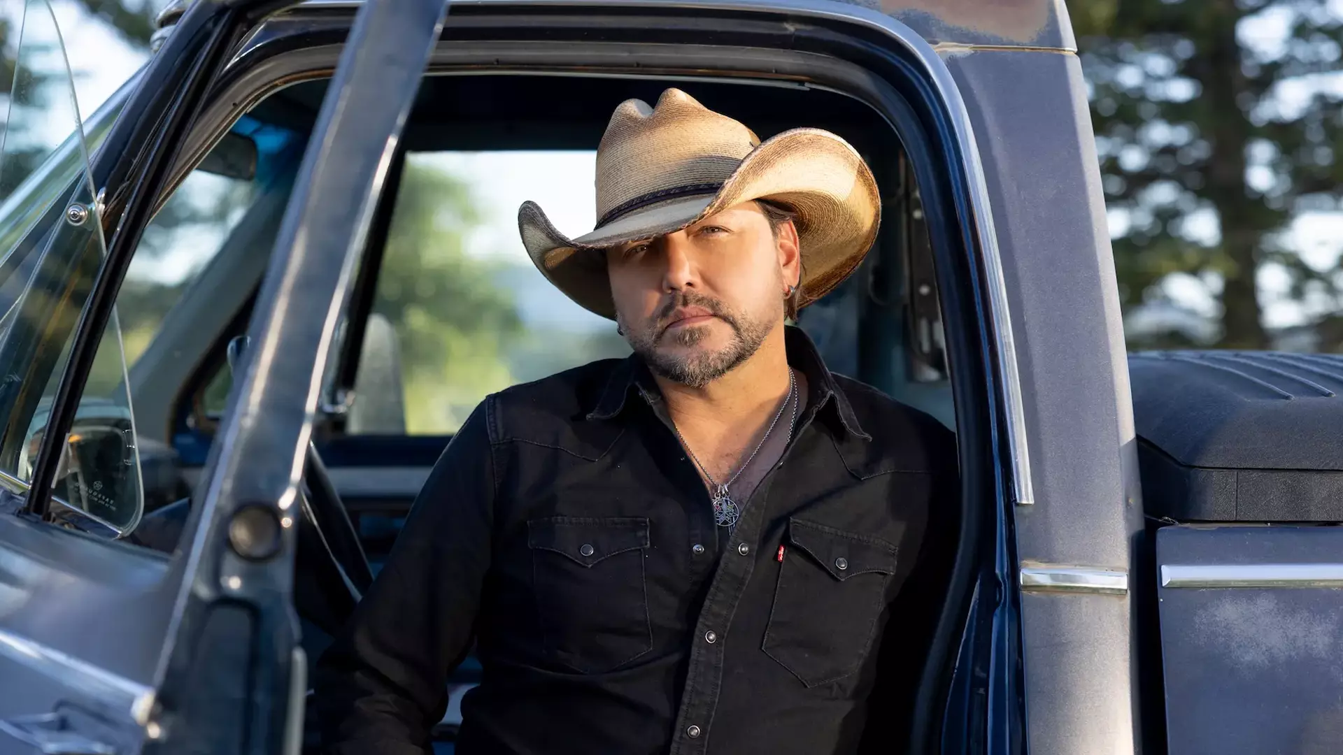 Jason Aldean leaning on a blue Truck