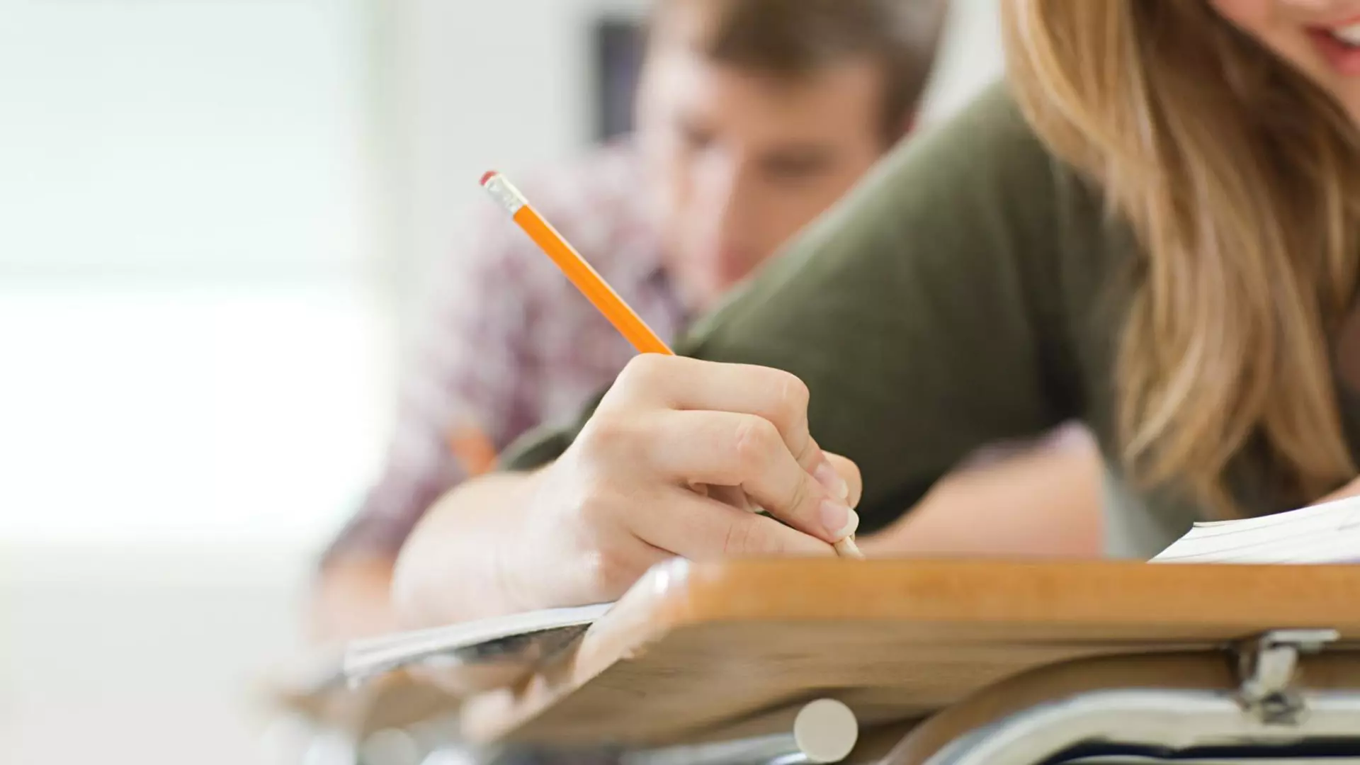 Eine Schülerin hält einen Bleistift in der Hand und schreibt etwas auf.