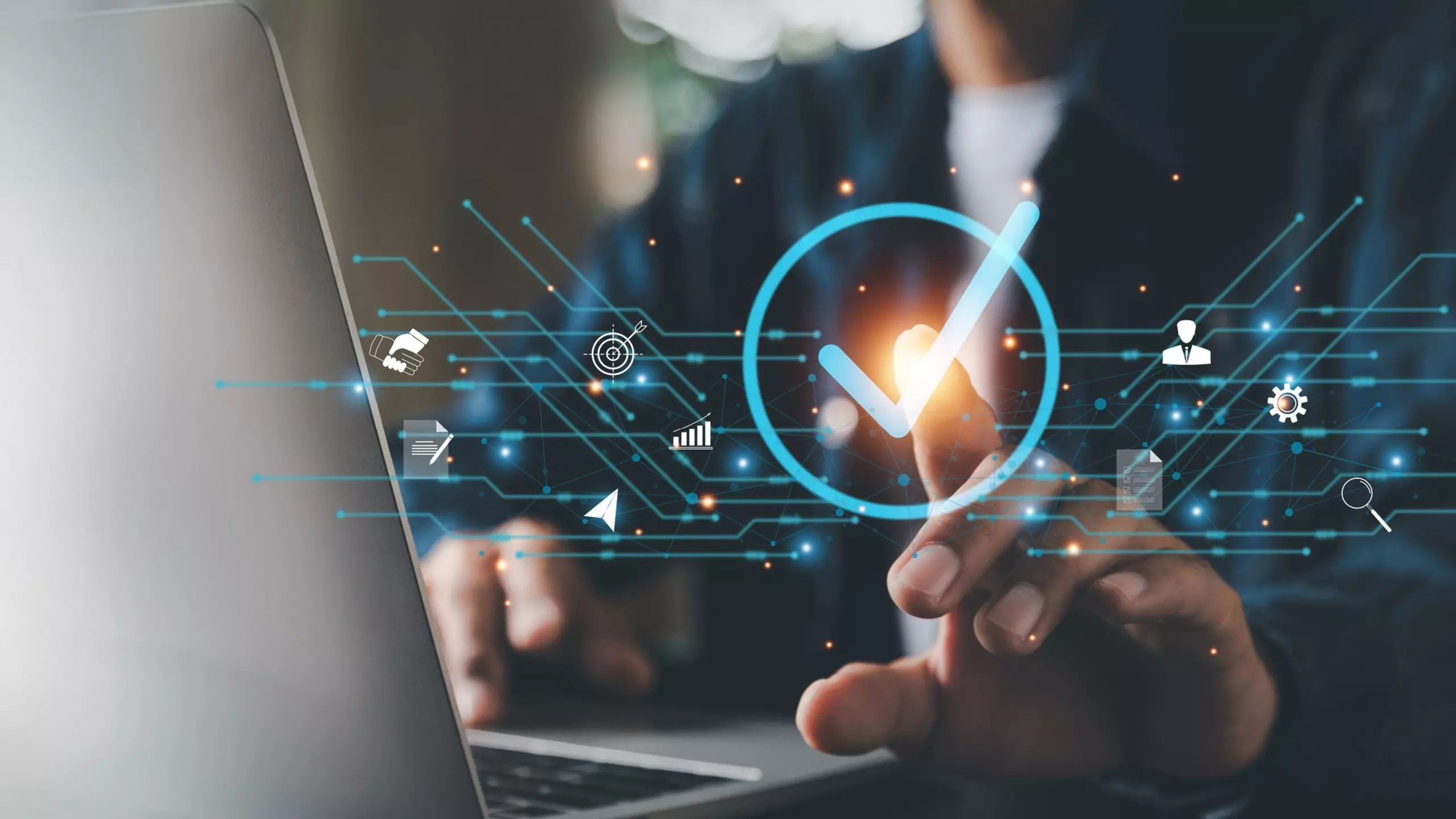 Hand tapping a digital checkmark symbol in front of a laptop.