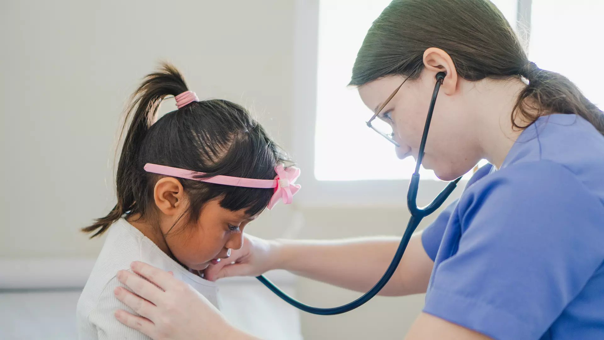 On the left, a girl is being examined by a nurse with a stethoscope.