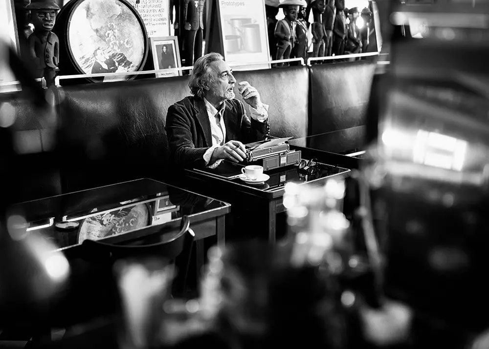 Person sitzt an Schreibmaschine in einem Café mit klassischer Einrichtung.