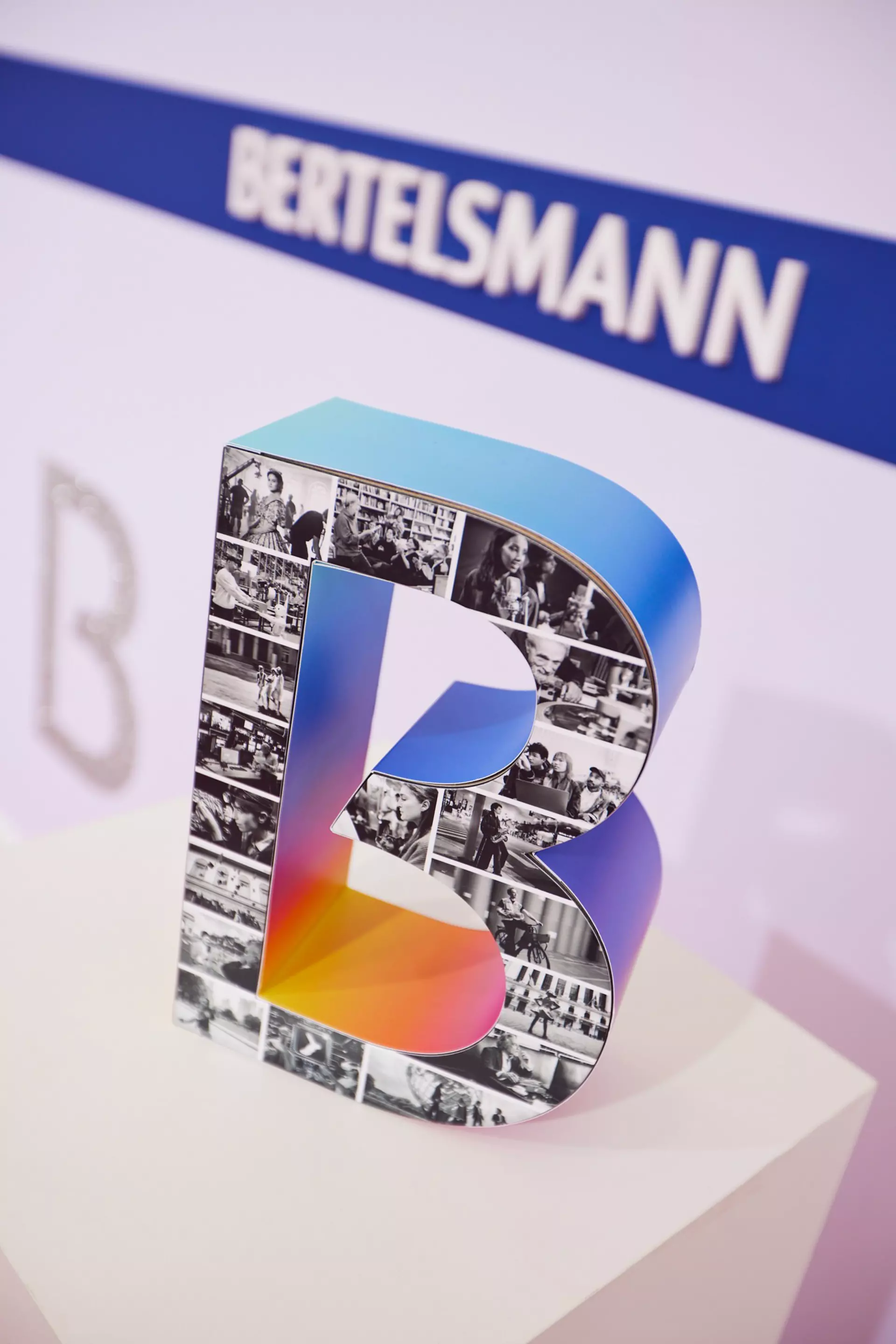 Ein Dekorationsaufsteller in B-Form mit einer Collage aus Fotos vom Starfotografen Jim Rakete mit dem Thema "Das alles ist Bertelsmann by Jim Rakete".