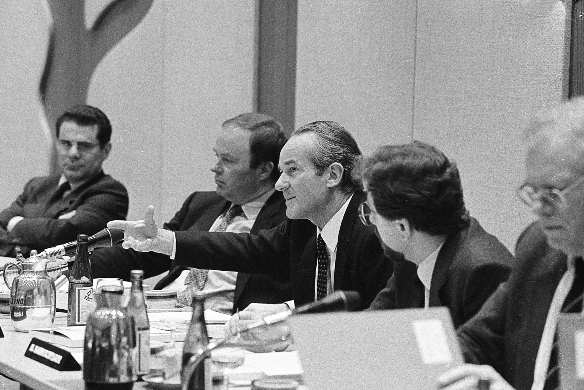 Five people are sitting at a long table with table microphones pointed at them. Reinhard Mohn sits in the middle and gestures with his right hand.