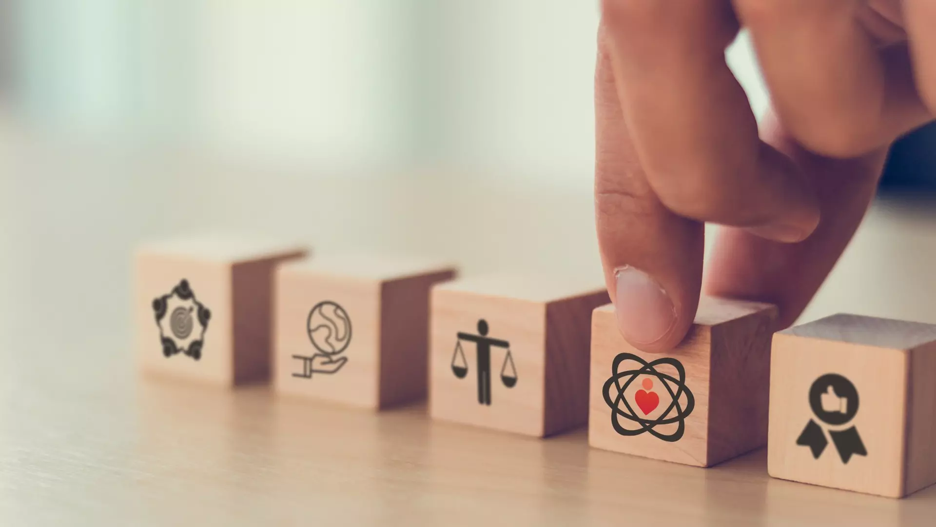 Finger berührt einen Holzblock mit Herz‑Symbol; weitere Blöcke zeigen Icons für Umwelt, Gerechtigkeit und Qualität.
