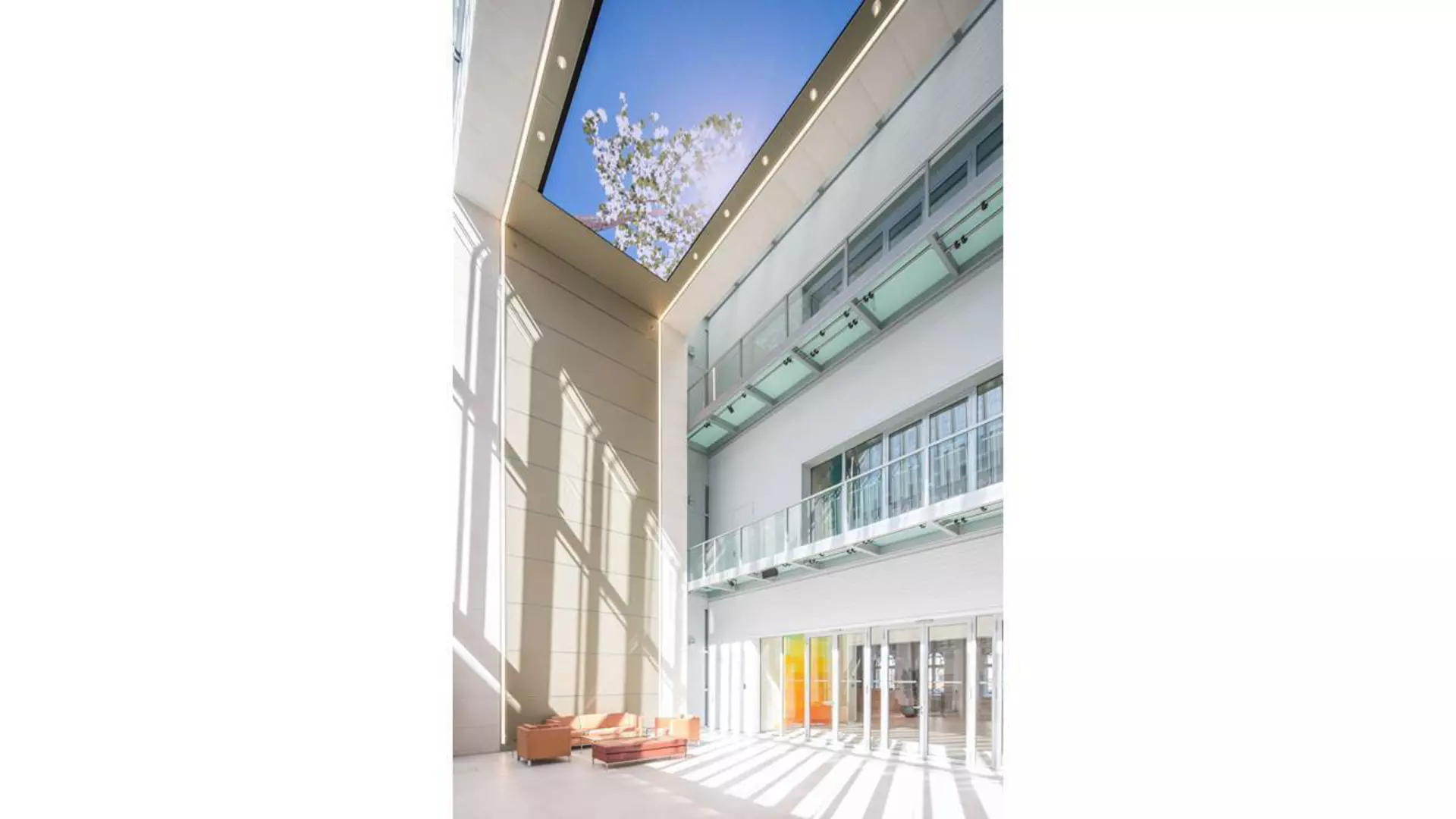 Heller, verglaster, sehr hoher Raum mit umlaufenden Galerien, bodentiefen Fenstern. Sitzmöbeln im Erdgeschoss und einem LED-Bildschirm an der Decke.