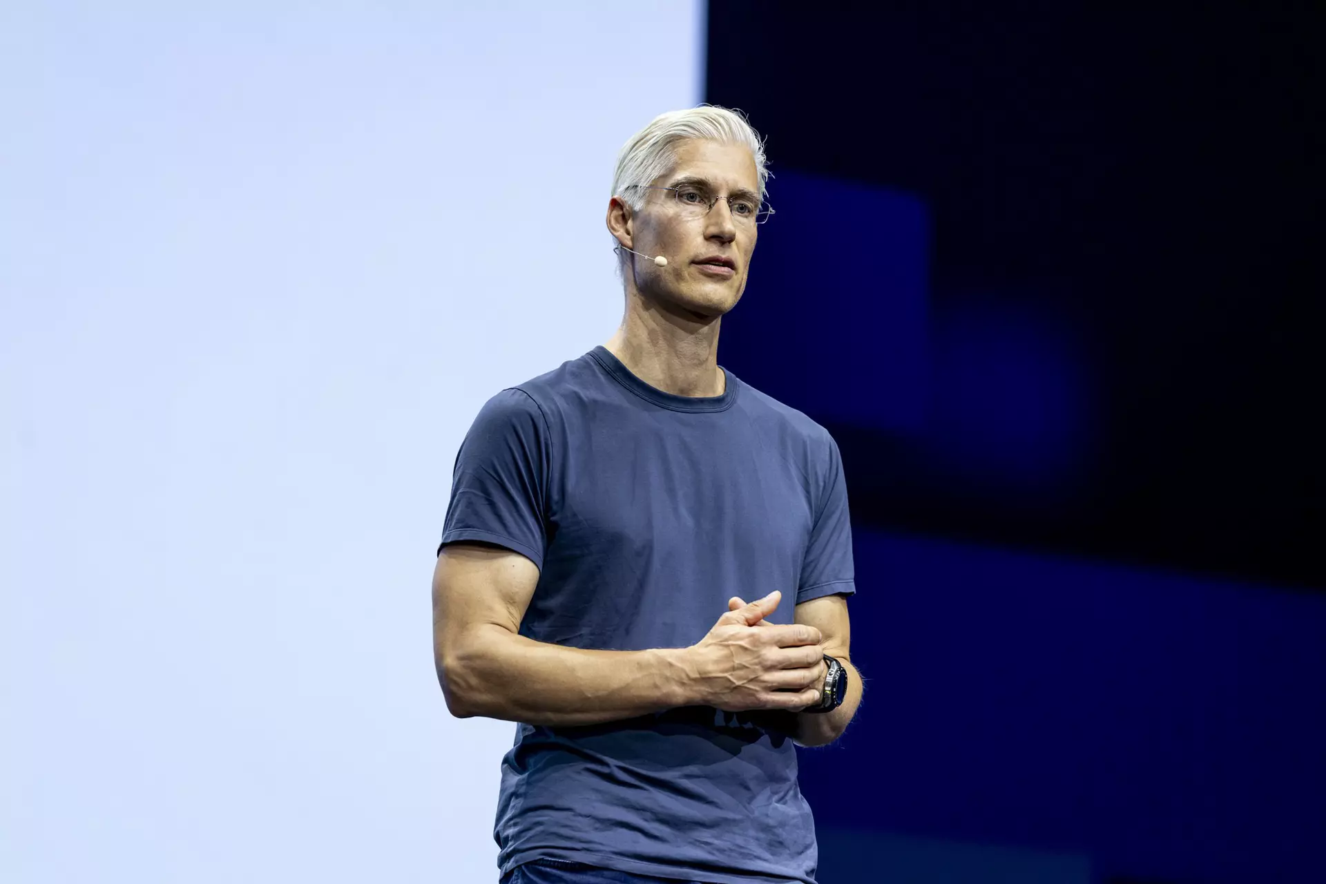 Person im T-Shirt steht auf Bühne vor hellem Hintergrund.