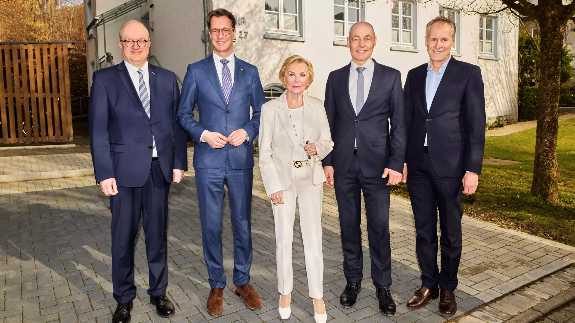 Four men in suits and a woman stand outside in front of a house