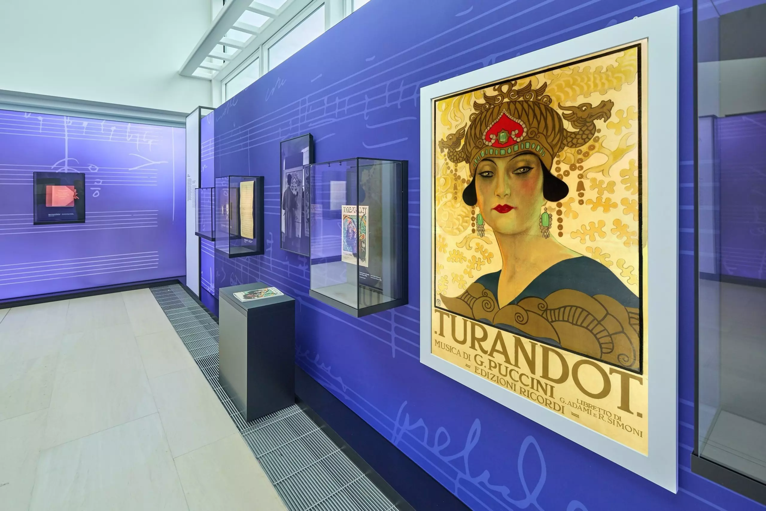 Numerous exhibits in glass display cases, with a replica of an old Turandot advertising poster in the foreground