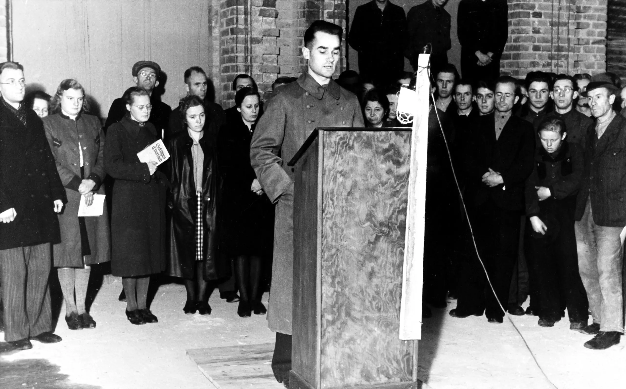 Reinhard Mohn is standing at a lectern; behind him, employees are listening while standing.