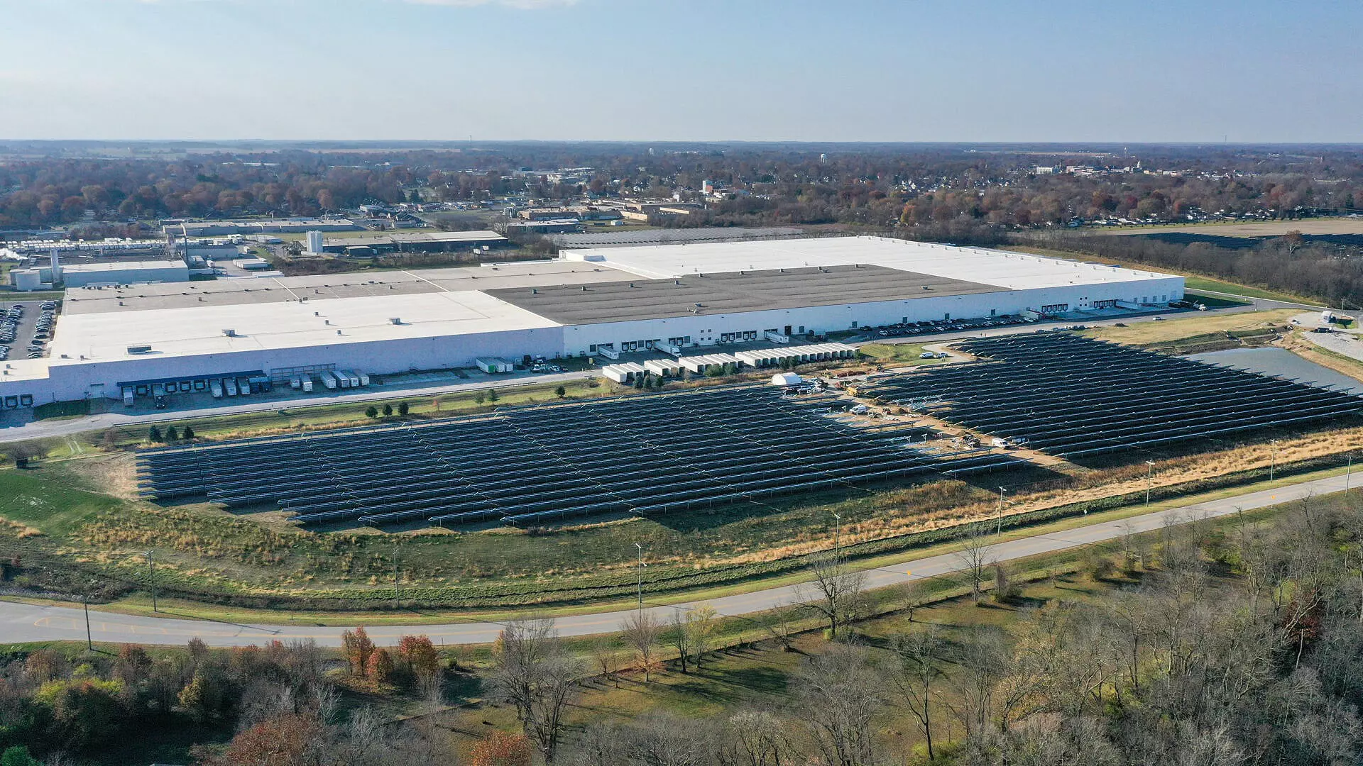 Aerial view of a large hall with many black solar panels in front of it.