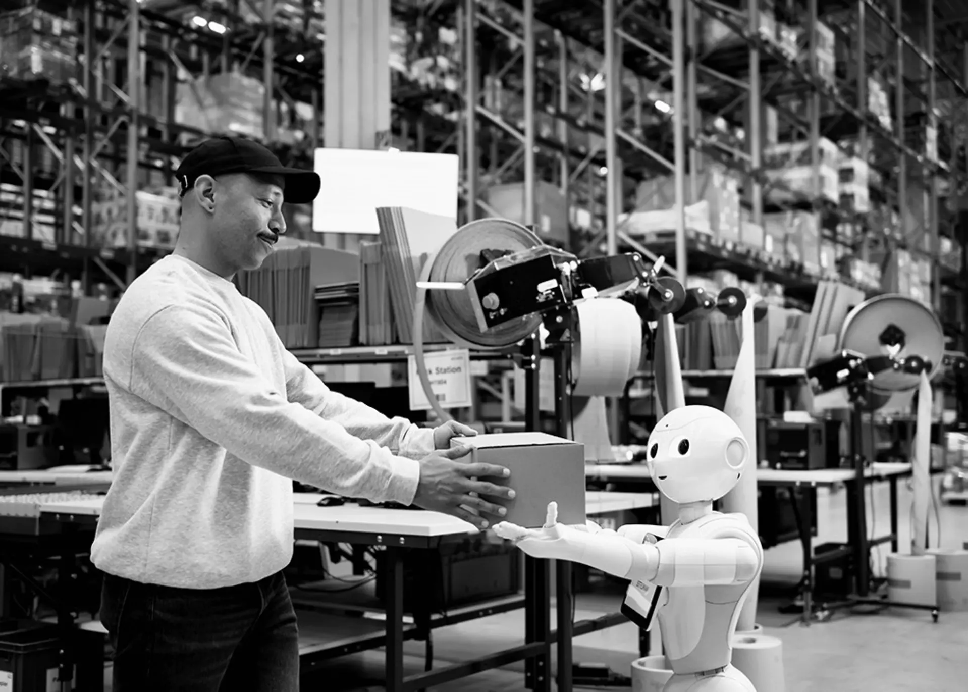 Person im Hochregallager übergibt einem kleinen Roboter ein Paket.