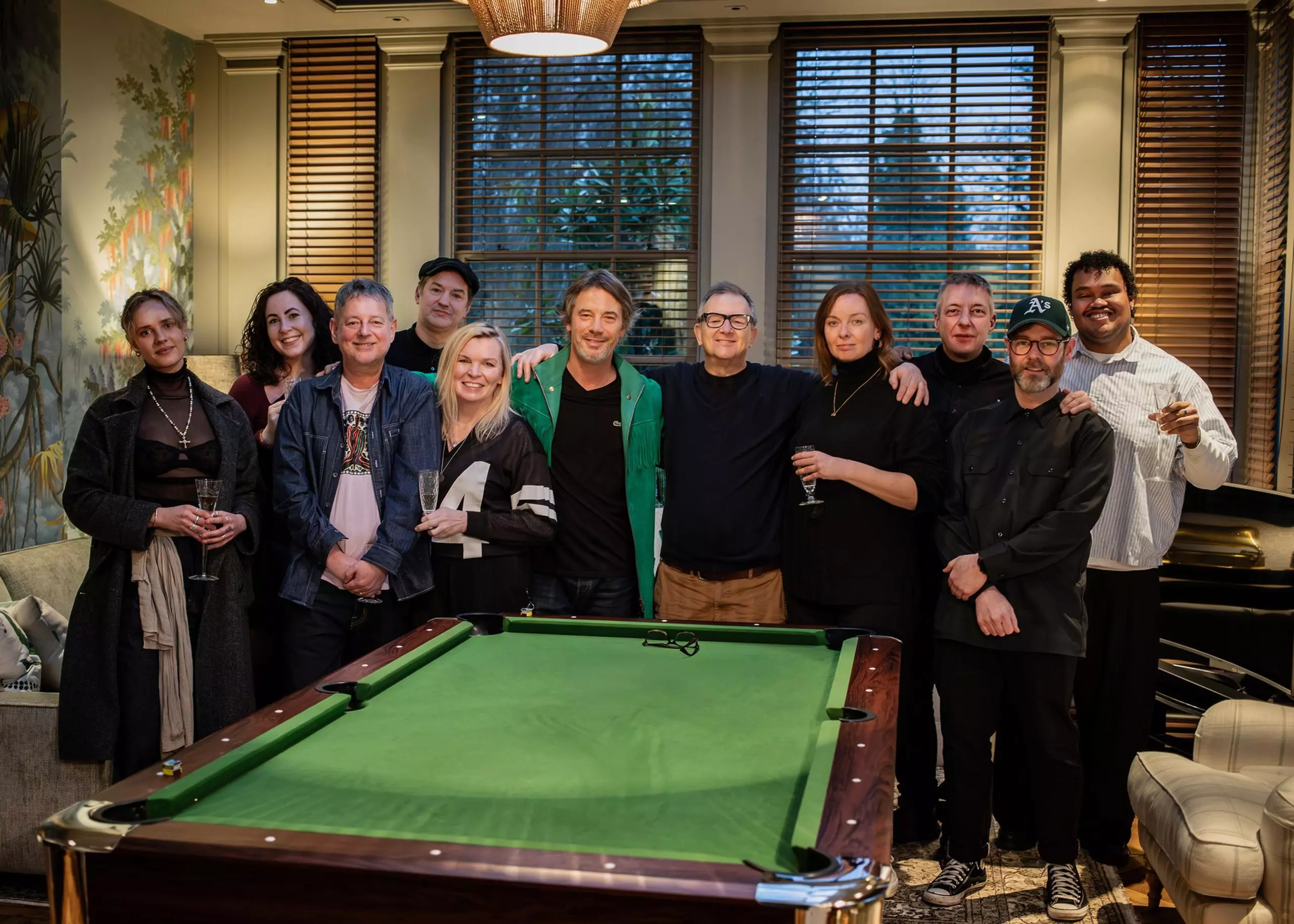 Eleven people stand in front of a billiard table. Some of them are holding champagne flutes in their hands.