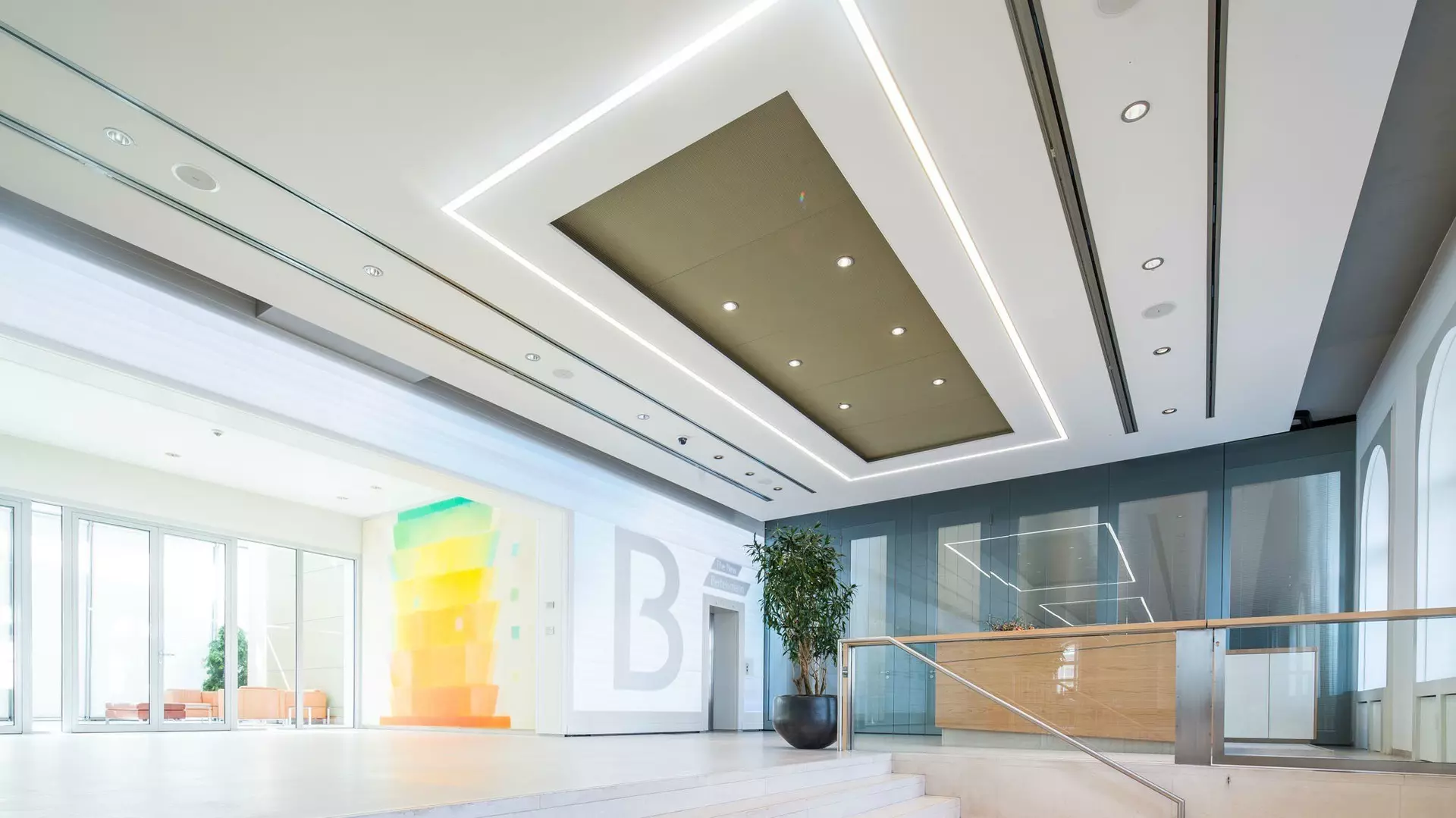 Großer moderner Innenraum mit Stufen, Glasgeländer, Sitzbereich, großem Gemälde in Spektralfarben und abgehängter Decke mit integrierter Beleuchtung.